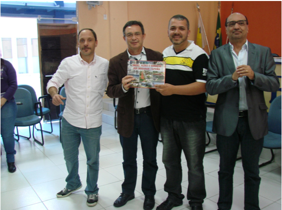 O trio de professores (André, Sabino e Jairo) entregando o livro de Itapema, ao aluno Luciano